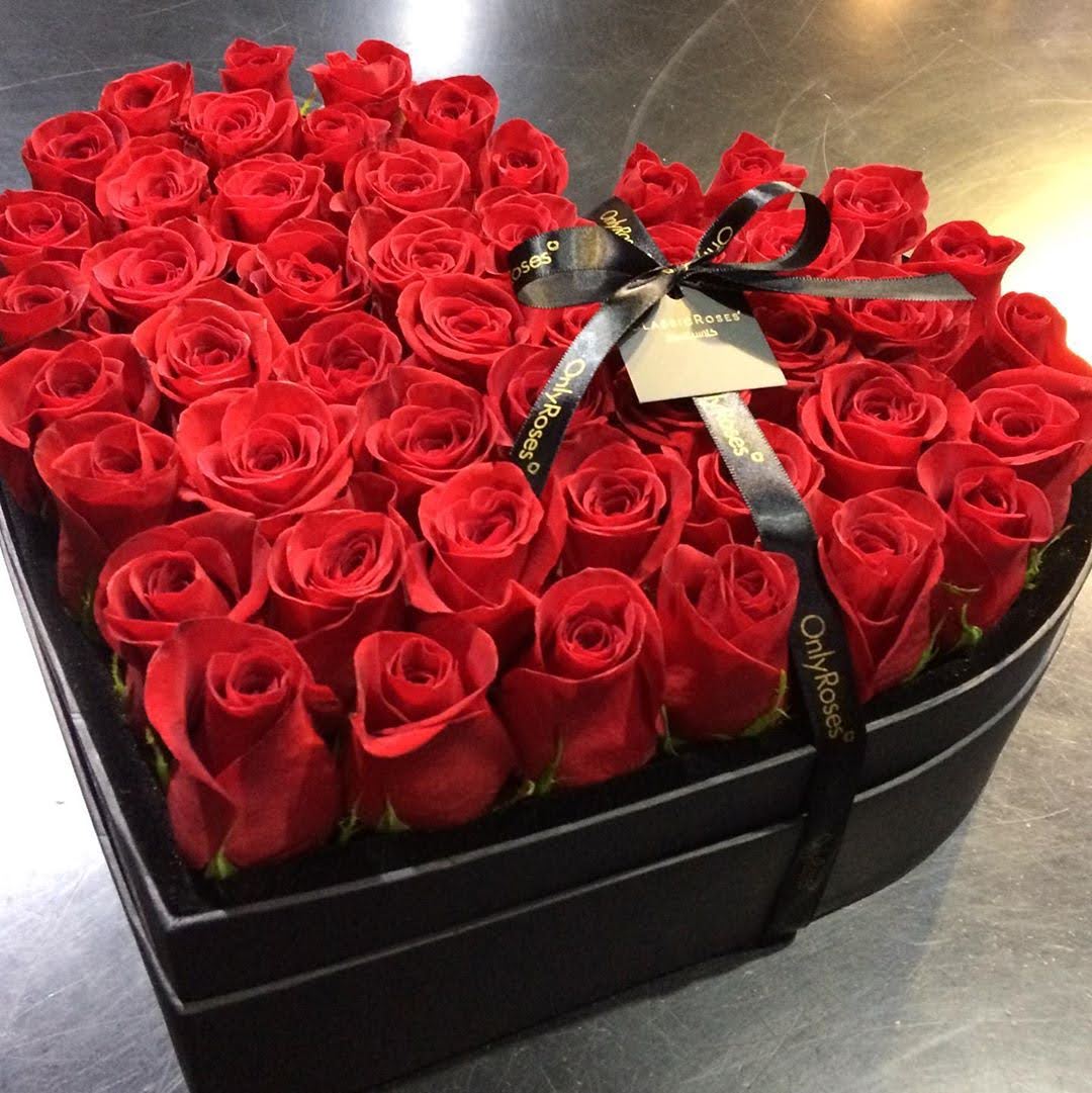 Heart-shaped box of red roses with a black ribbon on a reflective surface