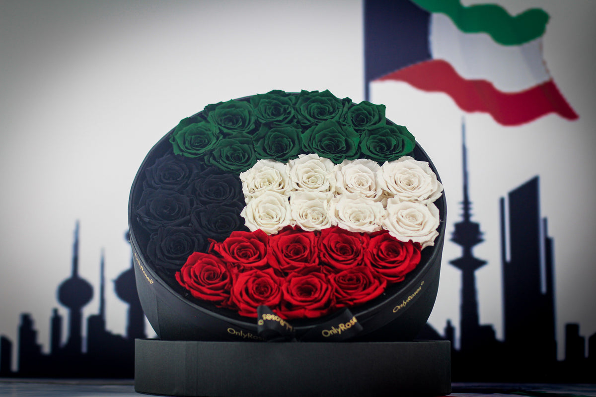 Round black box with green, white, and red roses arranged to resemble the flag of Kuwait against a cityscape silhouette.