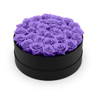 Black round box filled with purple roses on a white background