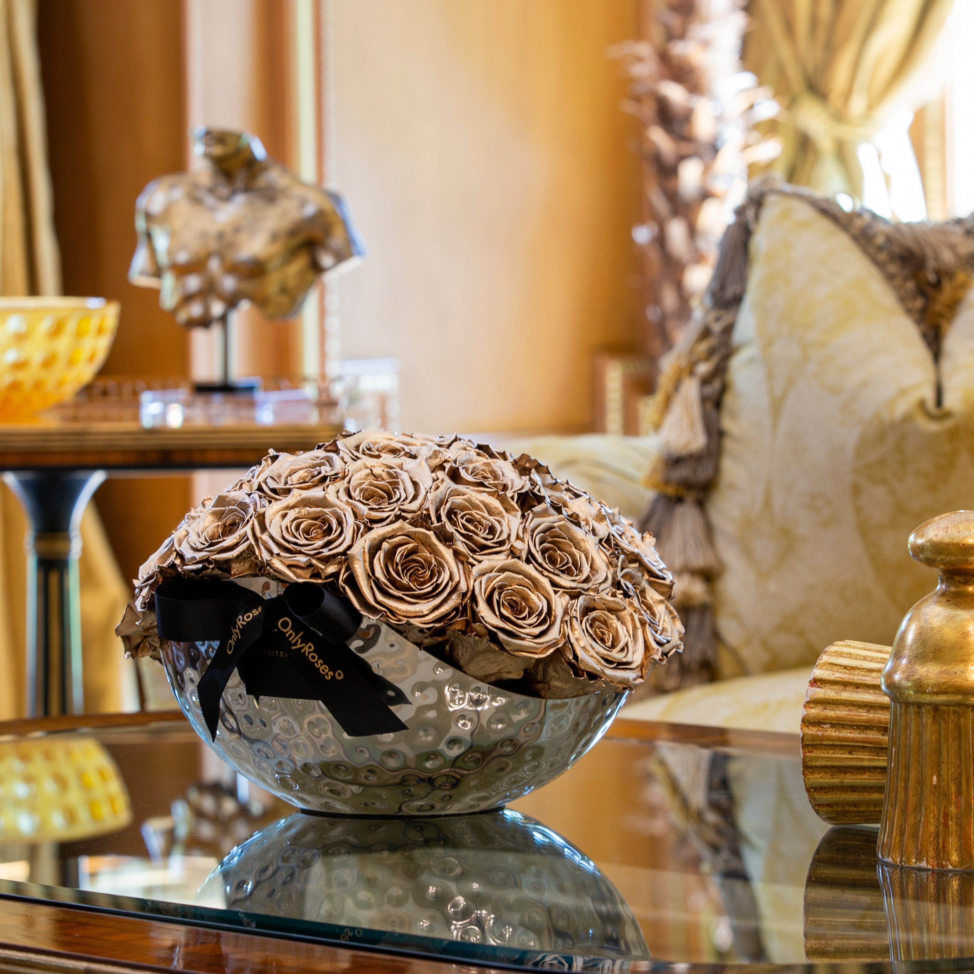 Decorative bowl with dried roses on a reflective surface in an elegant room.
